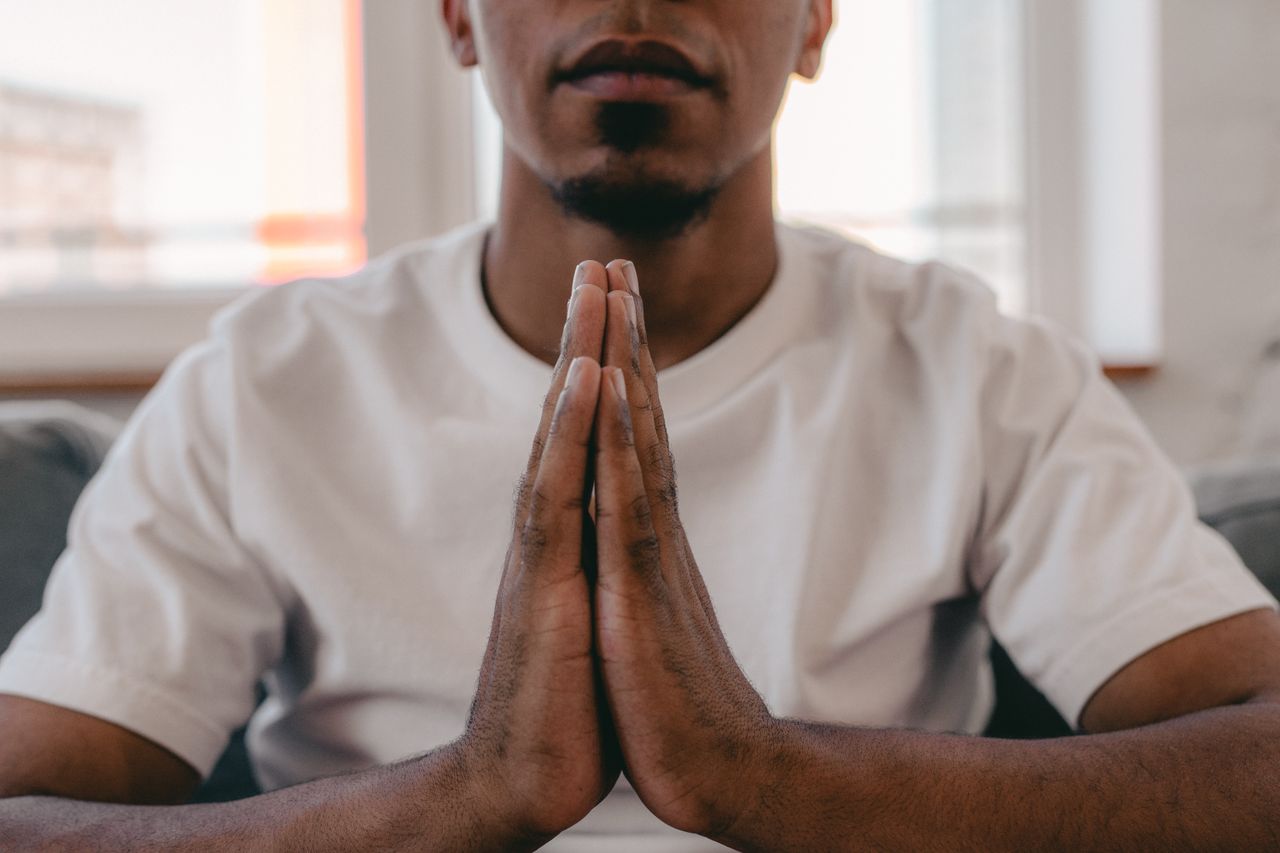 Close-up of a man clasping hands in prayer, indoor meditation setting.
