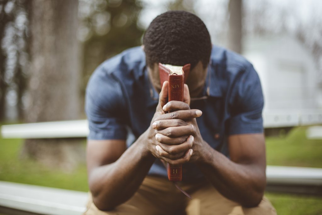 young african american male sitting with closed eyes with the bible in his hands